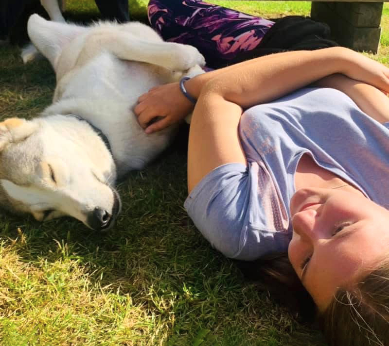Huskyfieber Feriencamp Junges Mädchen das mit einem Husky im Gras liegt und spielt